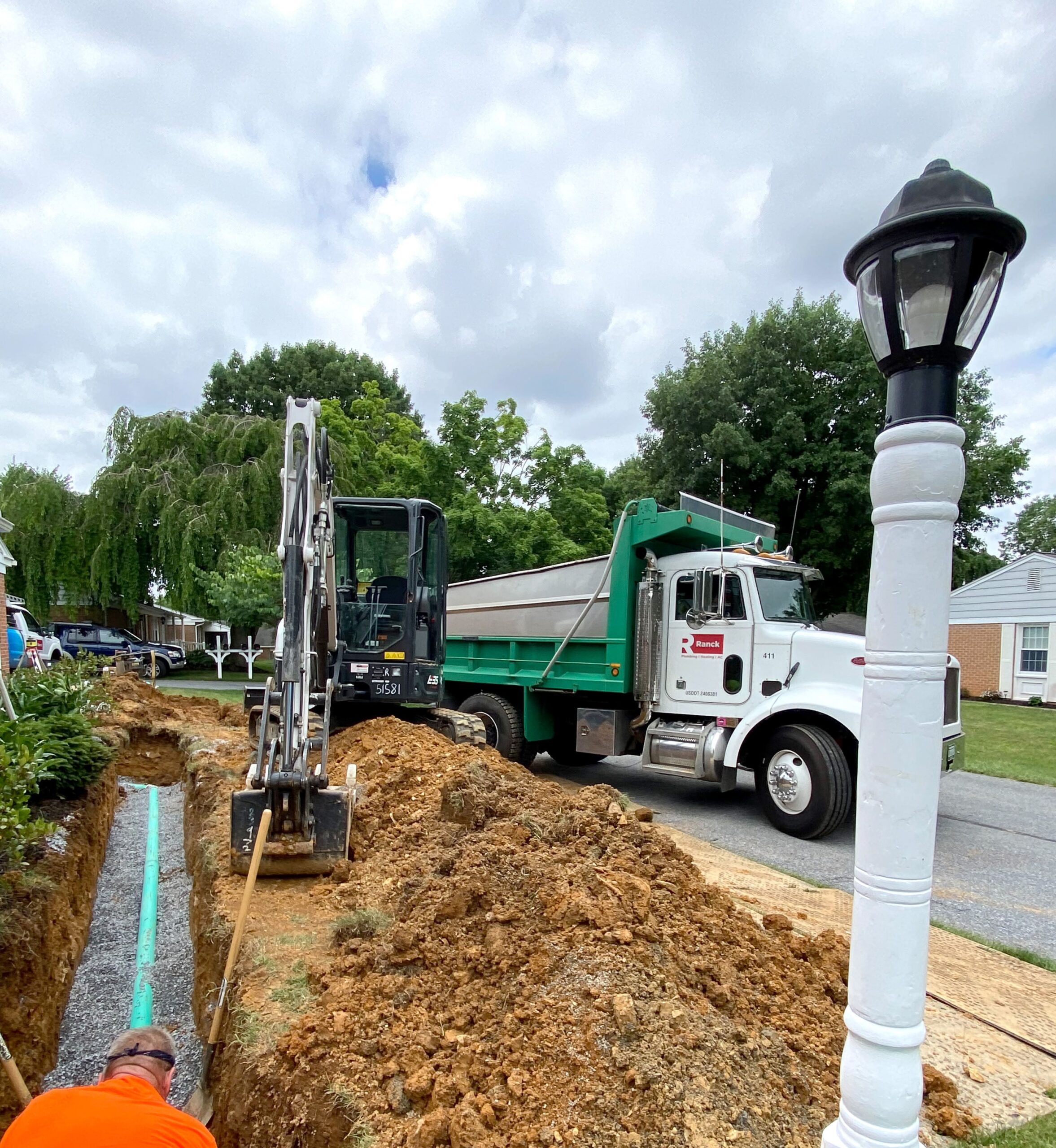 A Ranck dump truck and other heavy machinery digging out and repairing a sewer line. 